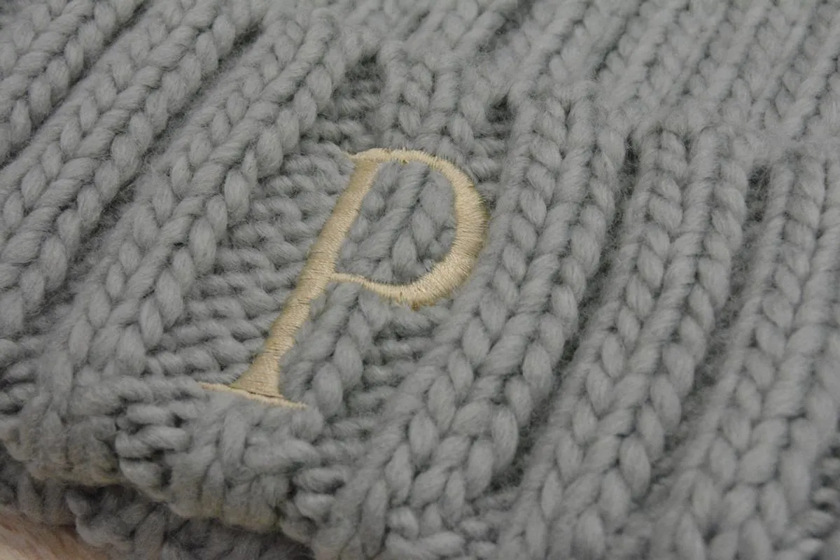 GORRO JUNIOR CON POMPóN DE PELO SINTéTICO COLOR GRIS  INICIAL BORDADA